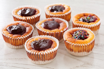 Seven delicious, homemade mini cheesecakes with berry jam in muffin cups on a wooden table