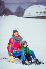 Fototapeta na wymiar The small boy and mother riding by sled along snow