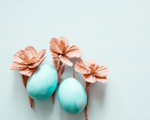 Easter eggs and decorative paper flowers on light background, top view, copy space