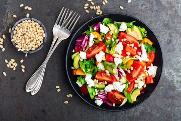 Vegetable dish, salad with avocado, pepper, tomato, italian mix, fresh lettuce, feta cheese and pine nuts. Healthy food. Top view