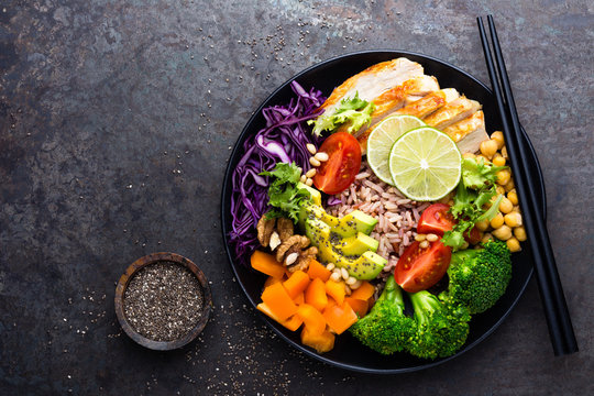 Buddha bowl dish with chicken fillet, brown rice, avocado, pepper, tomato, broccoli, red cabbage, chickpea, fresh lettuce salad, pine nuts and walnuts. Healthy balanced eating. Top view
