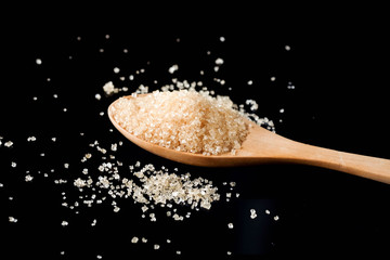 Brown sugar in wood spoon on black background.Components of The food is sweet delicious.