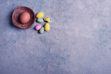 Group of colorful quail easter eggs with an big chicken brown one in nest