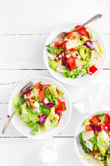 Healthy vegetable salad with fresh greens, lettuce, avocado, tomato, seet pepper and goat cheese. Delicious and nutritious diet dish for breakfast. Salad bowls on white wooden background. Top view