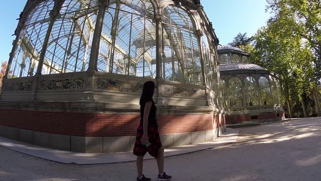 Pretty Girl Walking near Crystal Palace in Madrid Buen Retiro Park. Palacio de Cristal Building Made of Glass Metal in shape of Greek cross