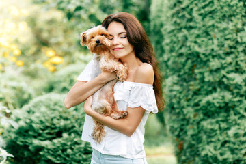 pretty young woman smiling happy with long dark hair in white dress holding small dog puppy yorkshire terrier
