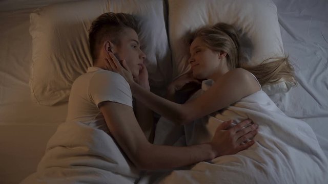 Happy young couple lying in bed at night and holding hands, strong relations