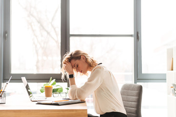 Tired young business woman sitting in office using laptop