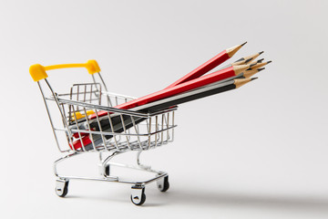 Close up of supermarket grocery push cart for shopping with yellow plastic handle filled with multi-colored pencils isolated on white background. Concept of shopping. Copy space for advertisement