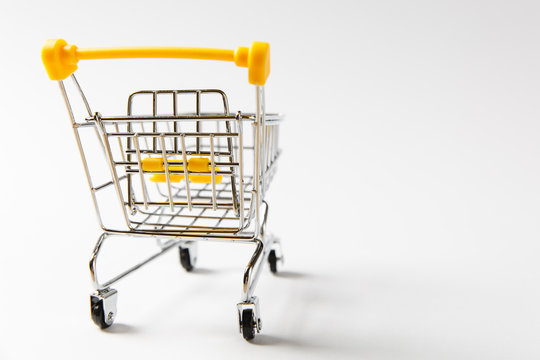 Close up of supermarket grocery push cart for shopping with black wheels and yellow plastic elements on handle isolated on white background. Concept of shopping. Copy space for advertisement