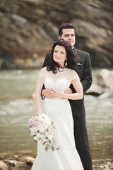 Beautifull wedding couple kissing and embracing near the shore of a mountain river with stones