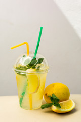 Natural lemonade with lemon and mint in a plastic cup with straws