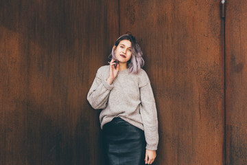 Young beautiful caucasian purple grey hair woman outdoor in the city leaning on colorful wall, looking camera, smiling - happiness, carefree, serene concept