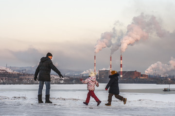 A man with children looks at a metallurgical plant polluting the atmosphere