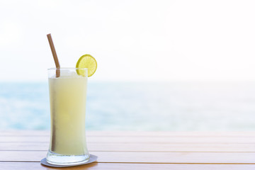 A glass of lemon juice on the brown wood table with seascape and sky background in the morning with vacation and relaxing time.