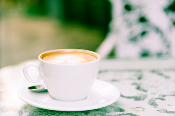 A white cup of coffee and silver spoon ready to served in the morning with relaxing and yellow lighting bokeh background.