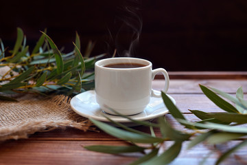 Чашка кофе с дымком, ветками эвкалипта, салфеткой из мешковины на деревянном коричневом фоне