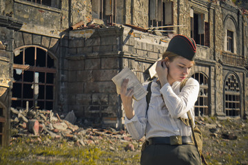 agirl in uniform on the background of the old destroyed building, with pages in hand