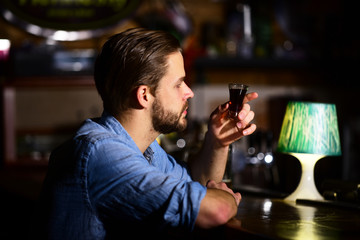 Man with beard drinks alcohol in bar on blurred background.