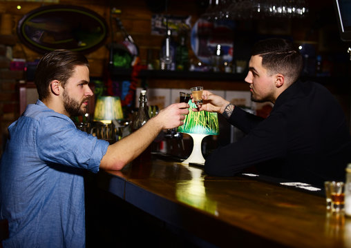 Barman drinks shot or liqueur with man in bar.