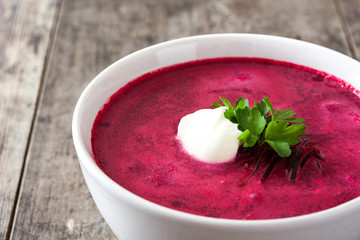 Beet soup in white bowl on wooden table