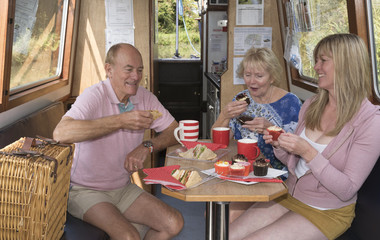 Holidaymakers enjoying afternoon tea of sandwiches and cakes aboard a narrowboat holiday afloat