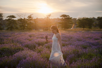 pretty young woman in dress with bouquet of flowers in lavender field at sunset in summer