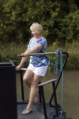 Woman using the tiller to steer a narrowboat along an English canal