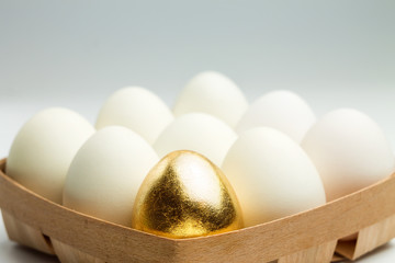 One golden egg among white eggs in a wooden box. Uniqueness concept.