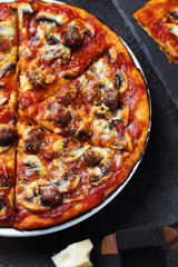 Homemade pizza with chorizo, mushrooms, mozzarella and pieces of chipolata sausages on dark table. Top view