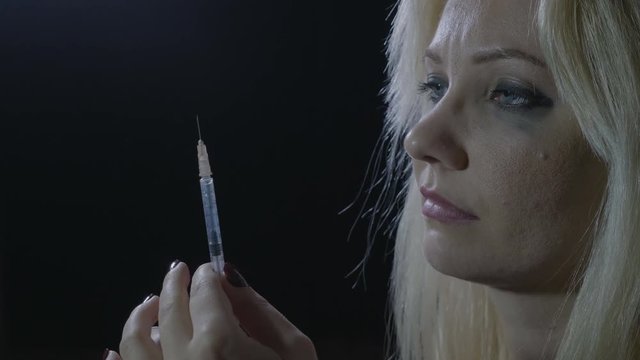 Close up of a young junkie blonde orphan girl preparing her daily drug dose of heroin injection