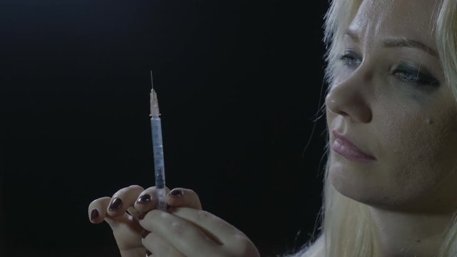 Portrait of a young female preparing syringe with heroin to surpass depression at home in a dark corner of the room