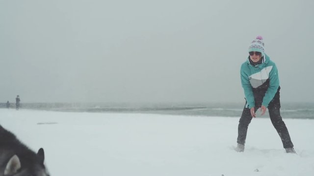 Young female playing and runing with siberian husky dog on the beach at snow storm, slow motion
