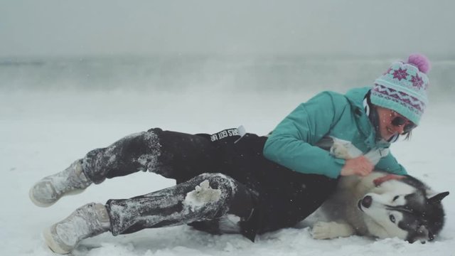 Young female playing with siberian husky dog on the beach at snow storm, slow motion