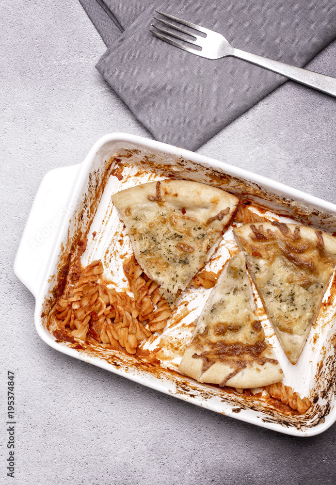 Wall mural dish of leftover pasta and cheesy garlic bread with a fork and napkin on a grey rustic background