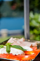 Delicious Italian antipasti platter with tomatoes, mozzarella cheese, basil and prosciutto (ham) at a lake for a romantic picnic