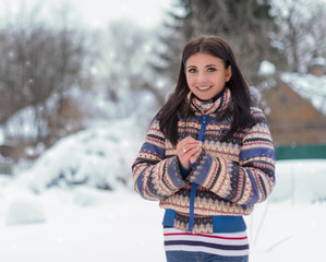 Fototapeta premium A young girl in a winter sports jacket smiles happily and tries to warm her hands, frozen from the cold