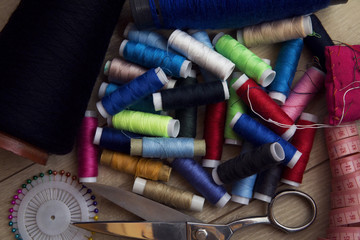 Colored tangles of thread, scissors, pins, centimeter and needle cushion on the leftt, on the rught is place for text. Items for sewing