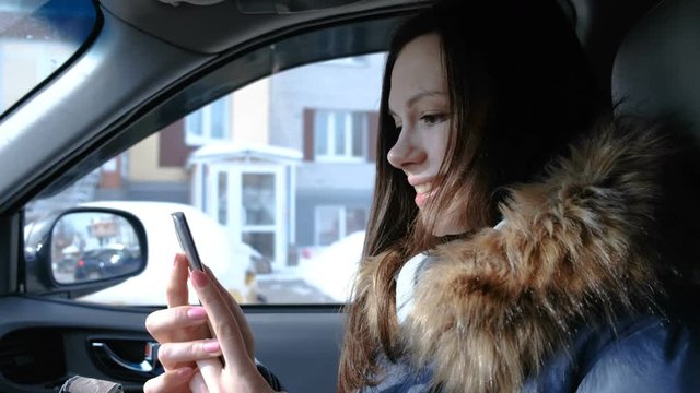 Woman in a car with a mobile phone. Young beautiful brunette woman looking something in the mobile phone and turns to the camera.