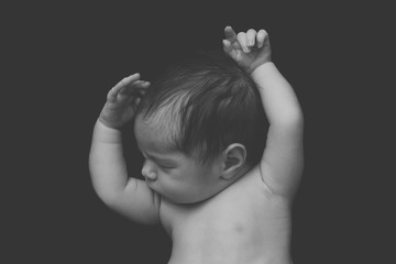 newborn baby boy asleep holding up his hands on a black background, black and white photo