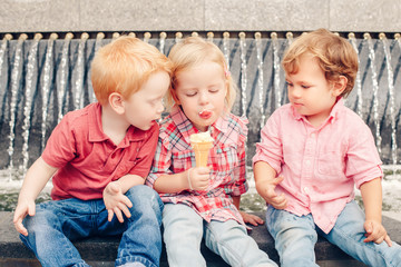 Group portrait of three white Caucasian cute adorable funny children toddlers sitting together sharing ice-cream food. Love friendship jealousy concept. Best friends forever.