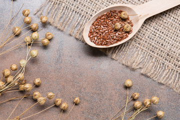 Fototapeta na wymiar flax seeds in a wooden spoon on a grunge surface, cloth burlap