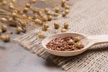 flax seeds in a wooden spoon on a grunge surface, cloth burlap