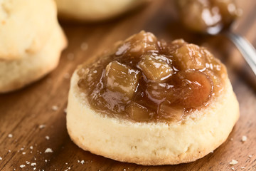 Homemade rhubarb jam on scone, photographed on wooden plate (Selective Focus, Focus one third into the jam)
