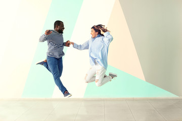 Cute interracial couple jumping against color wall