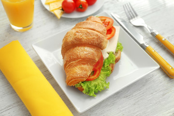 Plate with tasty croissant sandwich on table