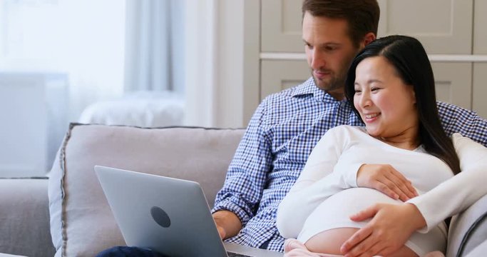 Pregnant couple using laptop on bed in living room 