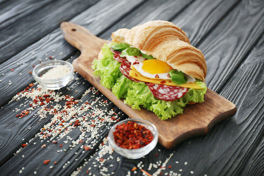Wooden board with tasty croissant sandwich on table