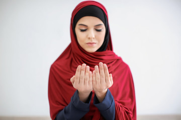 Young Muslim woman praying on light background