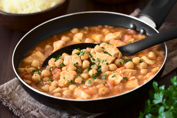 Chicken and chickpea stew or tagine in skillet, parsley on top, couscous in the back, photographed with natural light (Selective Focus, Focus in the middle of the image)
